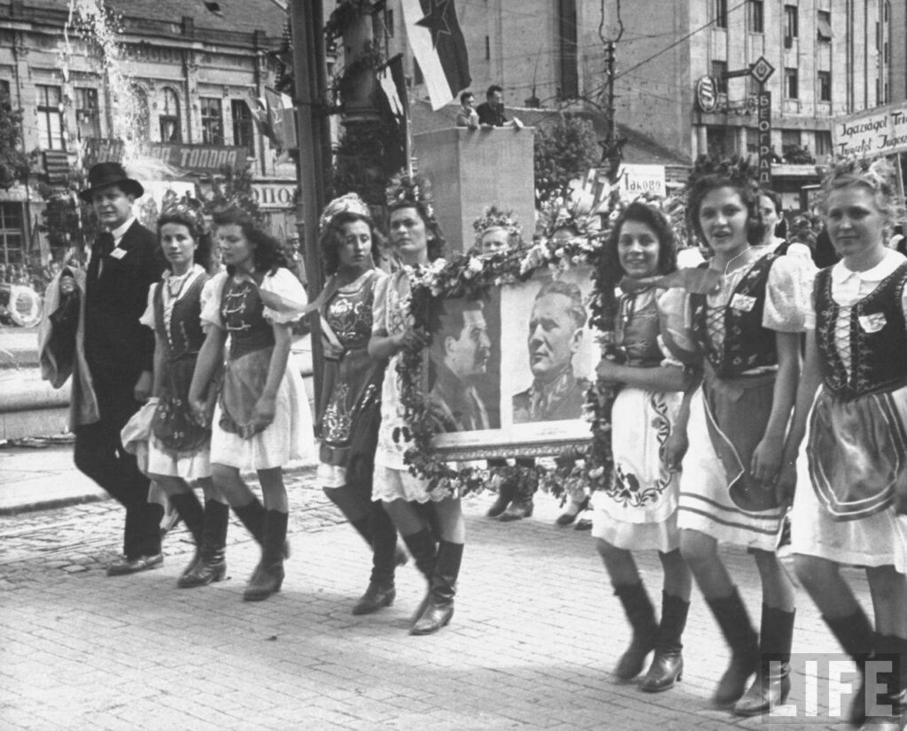 Frauen in Volkstracht tragen bei einem Umzug Porträts