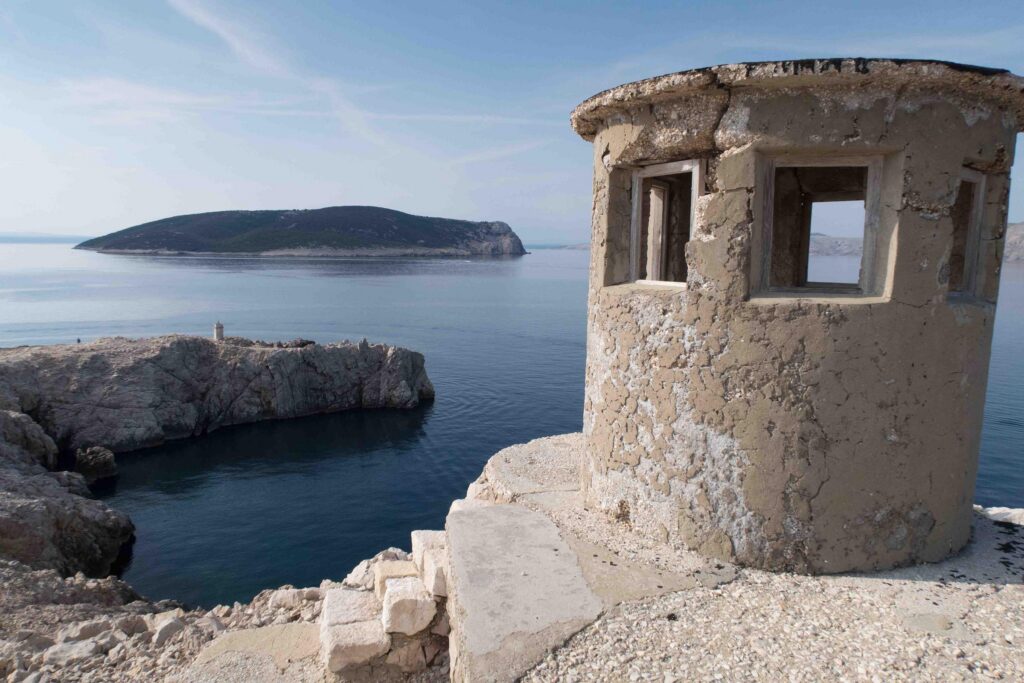 Runder steinerner Wachturm auf einer Landspitze, im Hintergrund eine kleine Insel