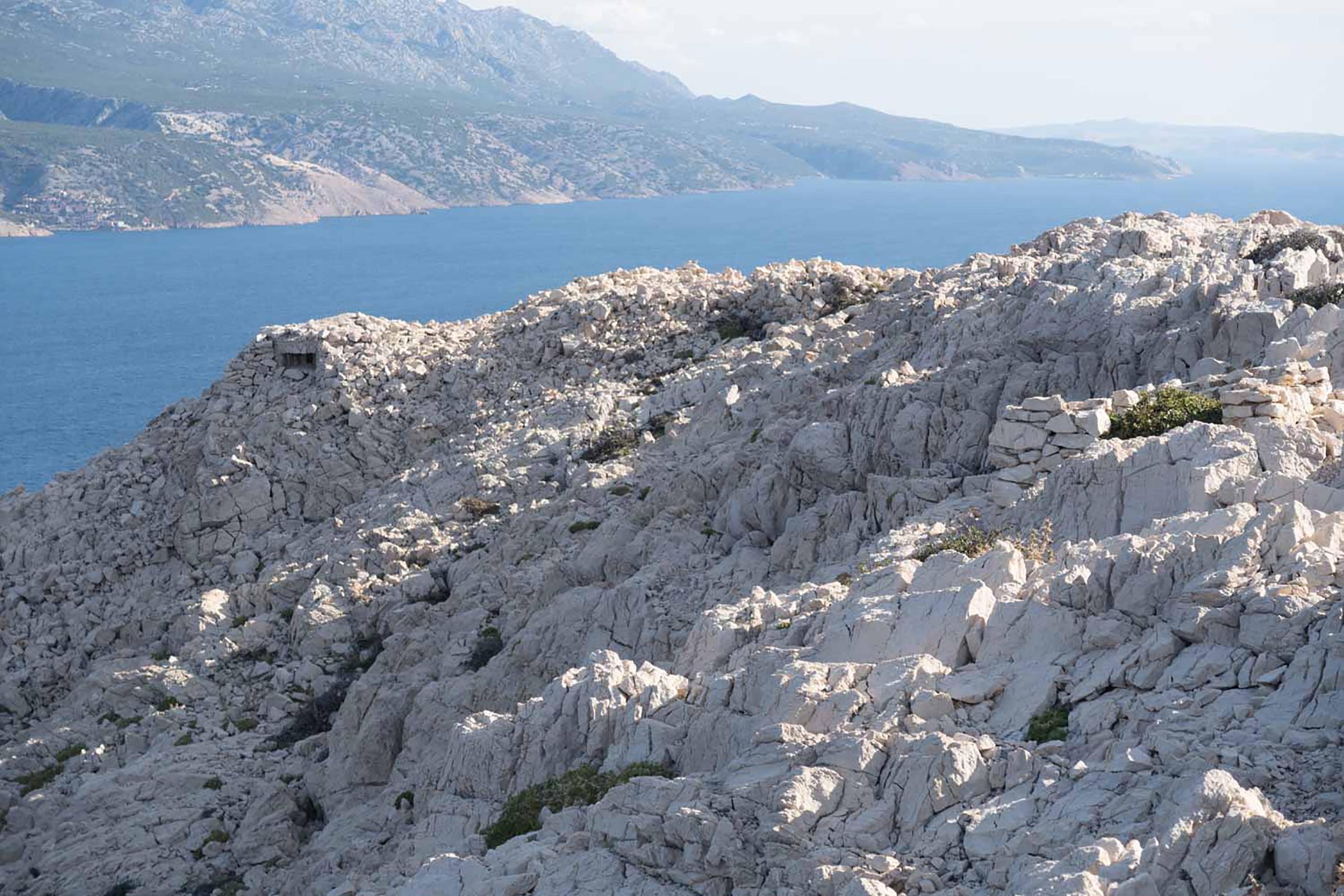 Kahler, felsiger Karst von Goli otok über dem Meer, im Hintergrund Berge