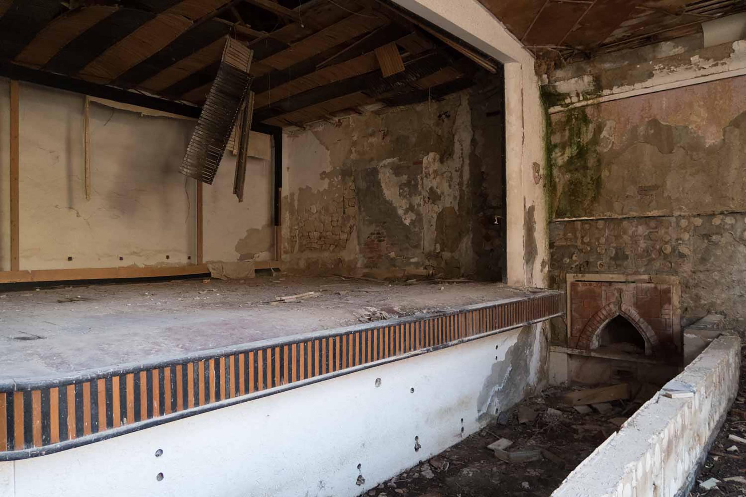 Verlassener Saal mit Bühne und beschädigten Wänden