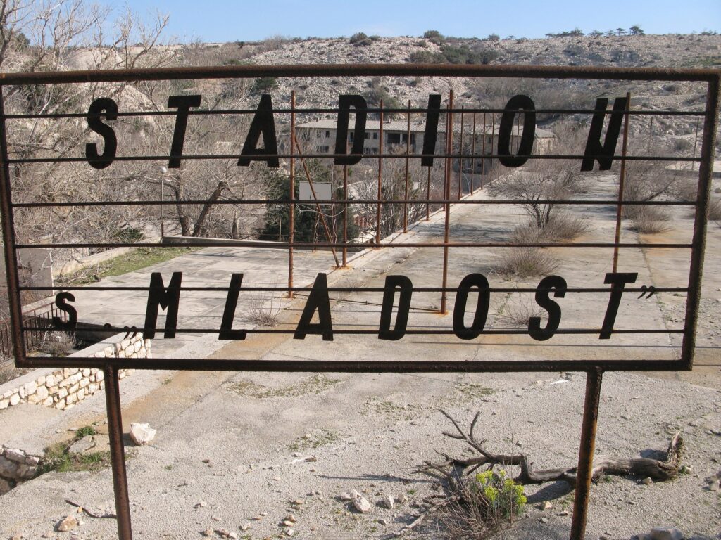 Metallschriftzug „Stadion Mladost“ über einem Sportplatz aus Beton